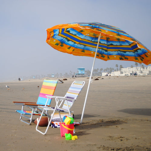 Northside of Huntington Beach, California with two beach chairs, an umbrella, beach towels, a beach blanket, football, and beach toys on the shore.